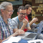 Three people collaboratively using laptop computers and smiling